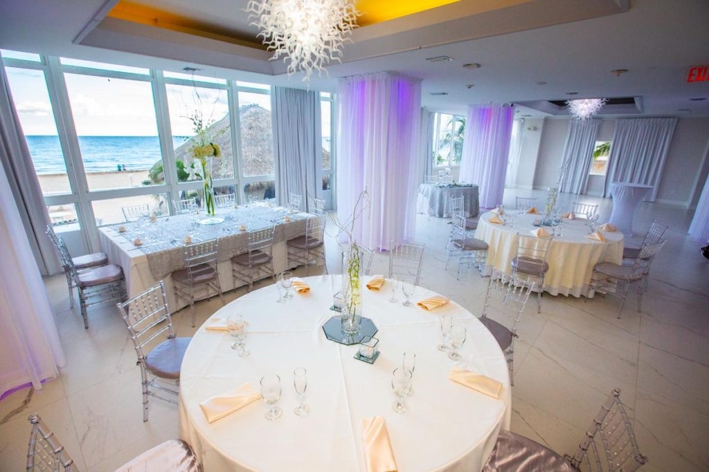 All-white oceanfront ballroom with reception tables and ocean views