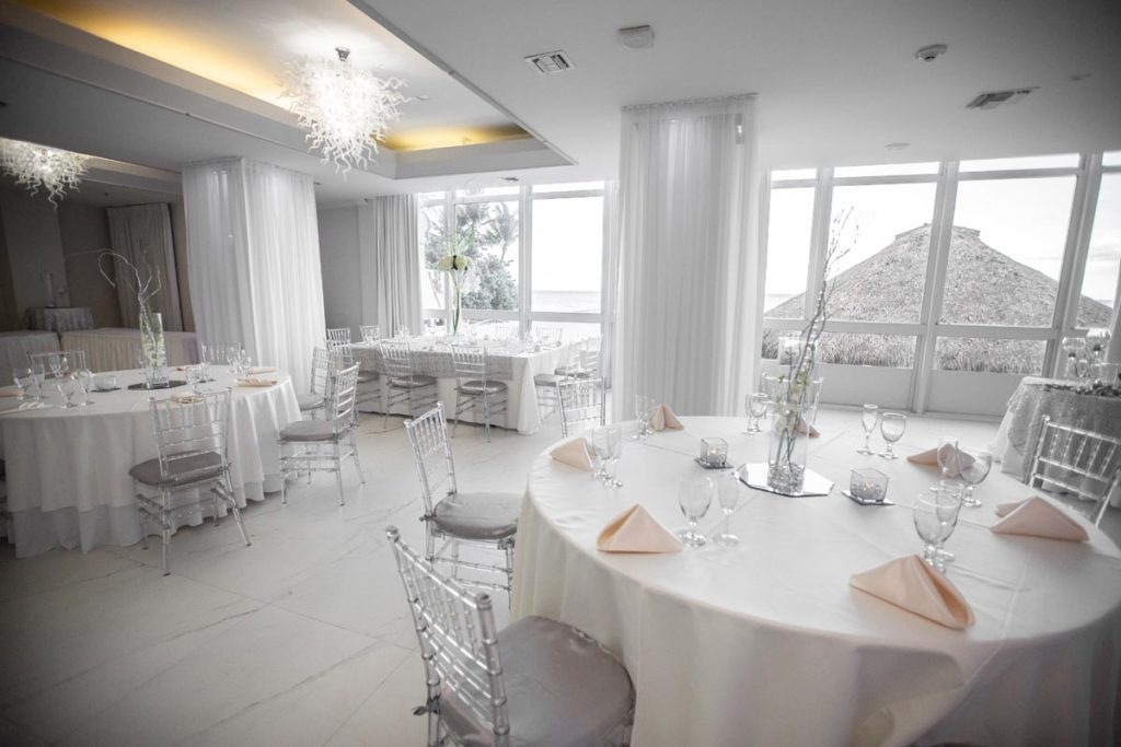 An inviting dining setup pairs soft white linens and sparkling glassware with the coastline just beyond the windows.