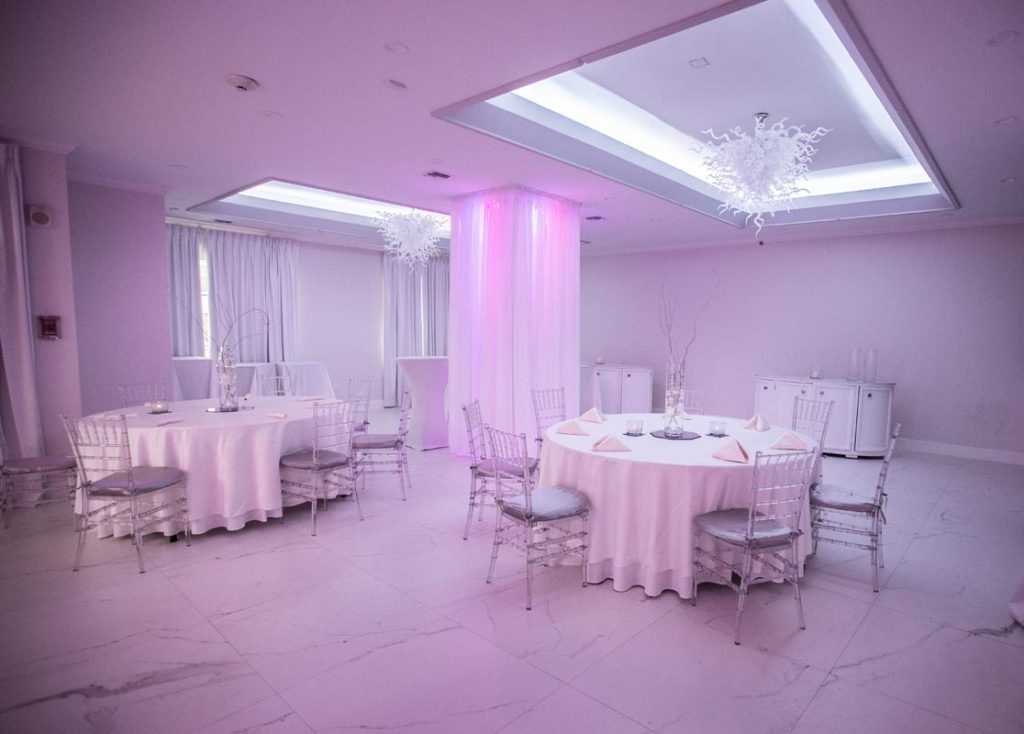 Soft pink lighting and white draping create an intimate evening mood beneath statement chandeliers.