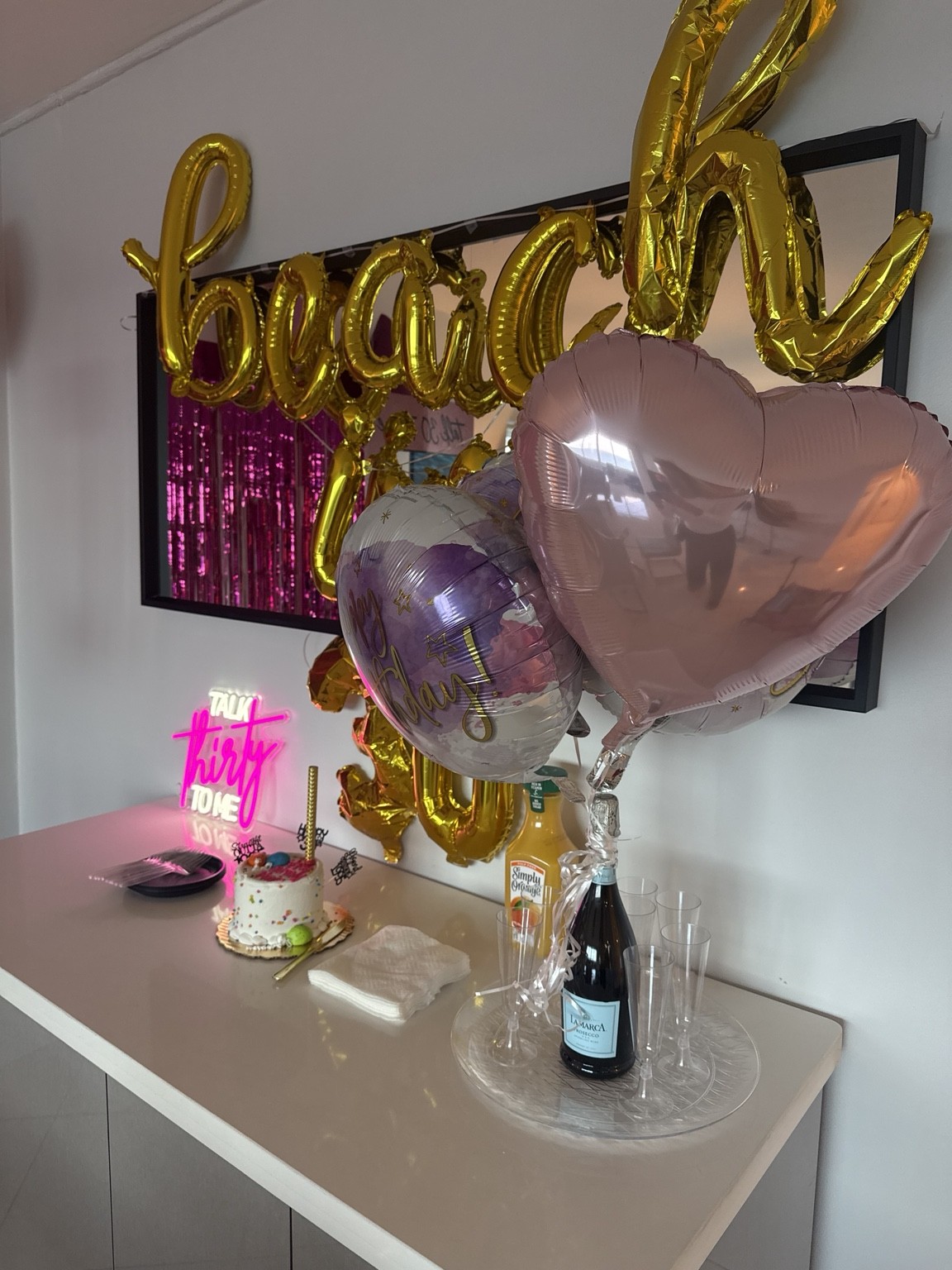 A birthday cake, bubbly and heart balloons make the celebration feel thoughtfully personal.